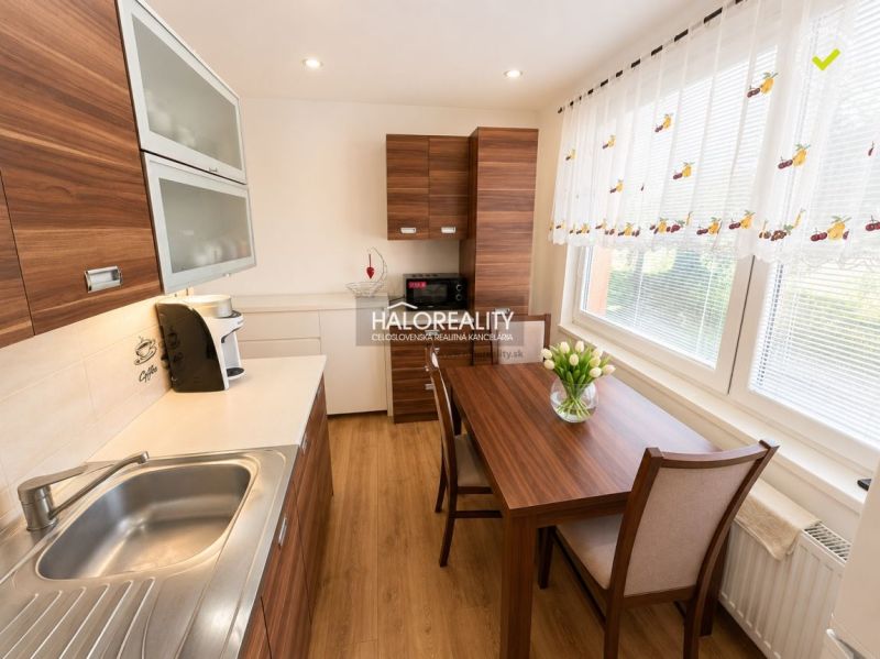 Küche in einer Einzimmerwohnung mit Holzdekor, Esstisch und sonnigem Fenster.