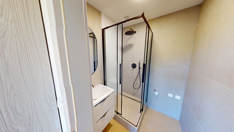 Badezimmer in einer 2-Zimmer-Wohnung mit verglaster Duschkabine und Waschbecken.