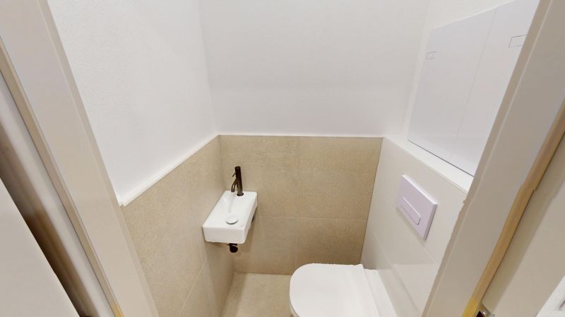 Toilette in einer 2-Zimmer-Wohnung mit Waschbecken und weißer Wand.