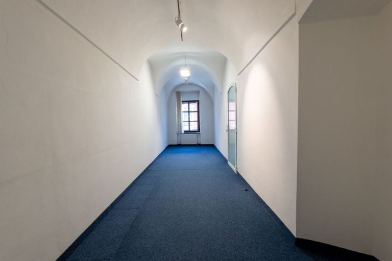 Ein enger Flur mit gewölbter Decke, Teppichboden und einem großen Fenster am Ende.