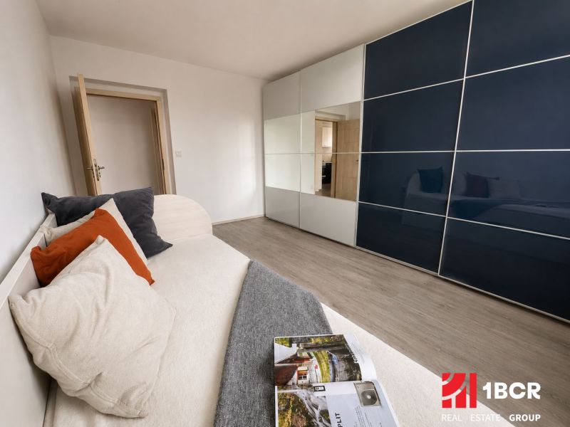 Innenraum einer 3-Zimmer-Wohnung mit Sofa, Einbauschrank und Boden mit Holzdekor.