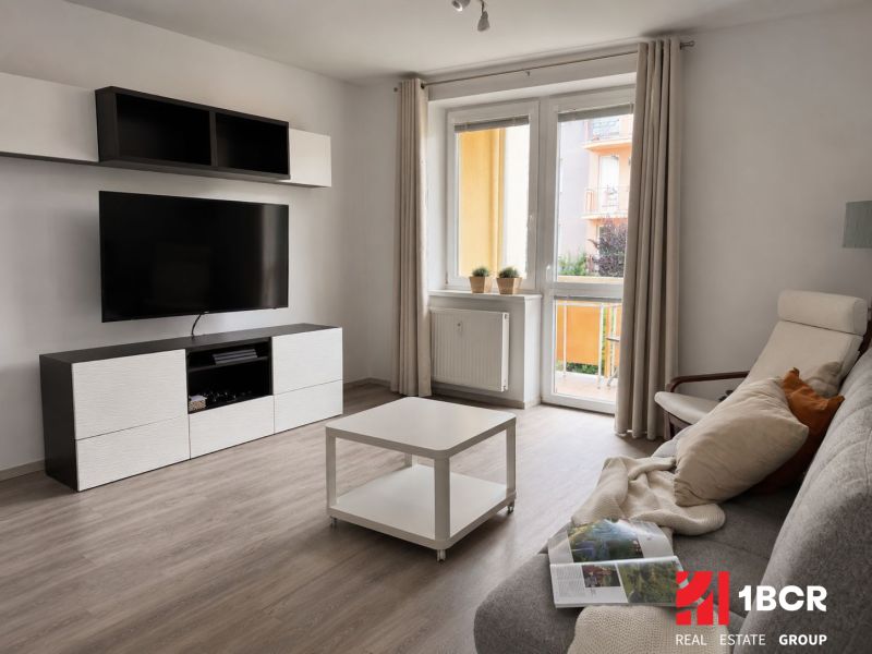 Wohnzimmer in einer 3-Zimmer-Wohnung mit Holzboden und einem Fernseher an der Wand.