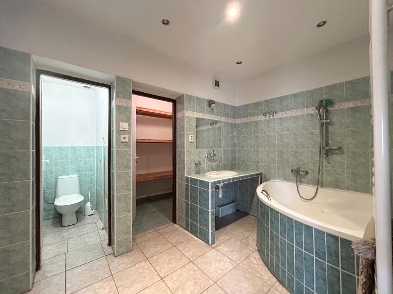 Badezimmer in einem Einfamilienhaus mit Badewanne, grünen Fliesen und Zugang zur Toilette.