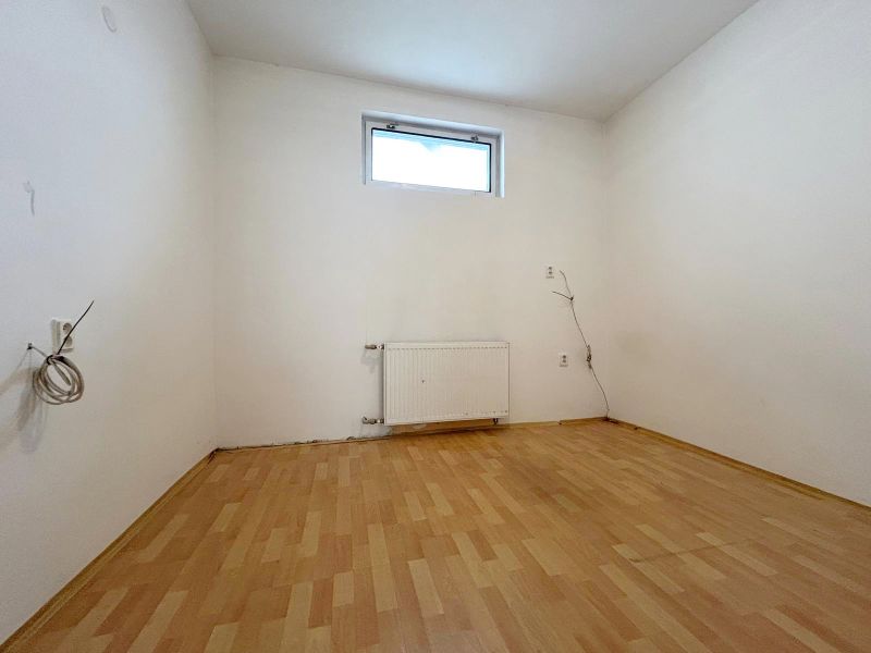 Ein Zimmer in einem Einfamilienhaus mit einem Boden in Holzoptik und einem Heizkörper unter dem Fenster.