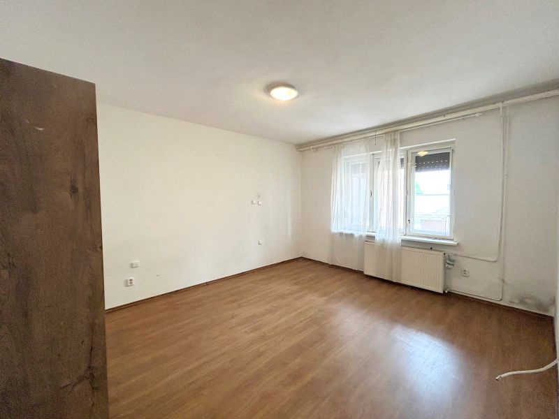 Ein Zimmer in einem Einfamilienhaus mit einem Boden in Holzoptik und Fenstern mit weißen Vorhängen.