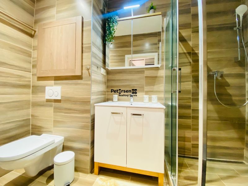 Badezimmer in einer 2-Zimmer-Wohnung mit Waschbecken, Duschkabine, Toilette und Holzdekor.