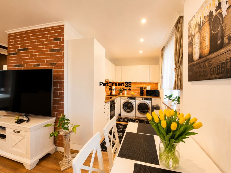 Innenraum einer 2-Zimmer-Wohnung mit weißen Möbeln, Ziegelverkleidung und Boden in Holzoptik.