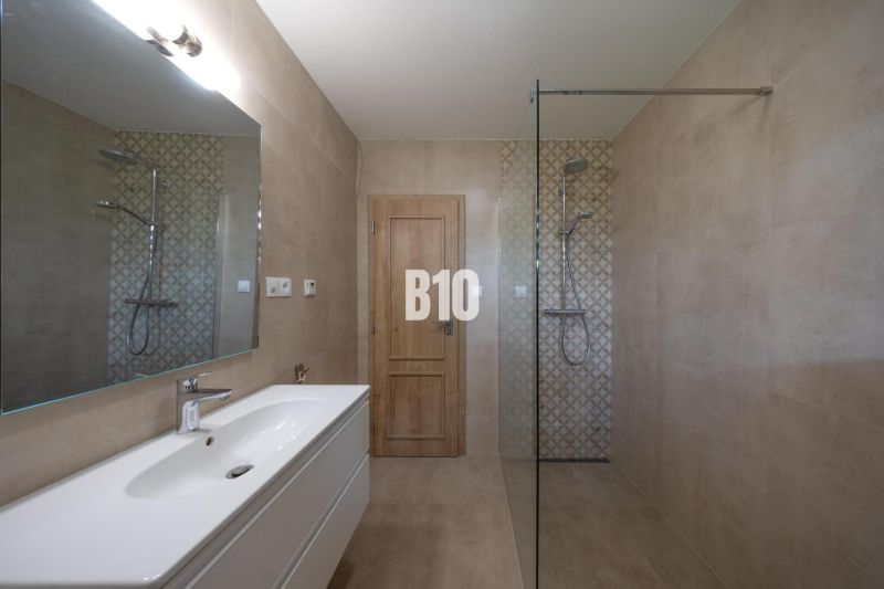 Modernes Badezimmer mit großem Spiegel, Duschkabine und minimalistischer Ausstattung.