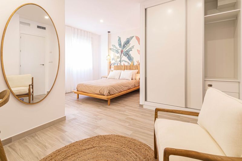 Innenraum einer Ferienwohnung mit Bett, Spiegel und Boden in Holzoptik.