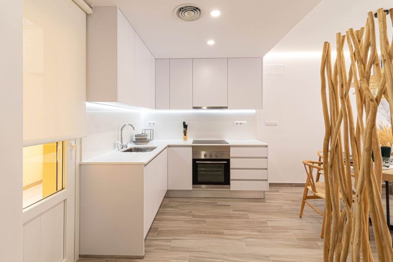 Küche in einer Ferienwohnung mit weißen Schränken und einem Boden in Holzoptik.