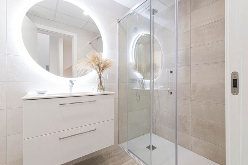 Badezimmer in der Ferienwohnung mit großem beleuchtetem Spiegel und Duschkabine.