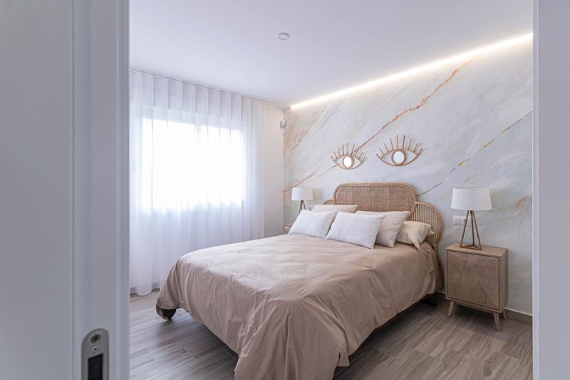Schlafzimmer in einer Ferienwohnung mit Bett, Stoffvorhängen und einem Boden in Holzoptik.