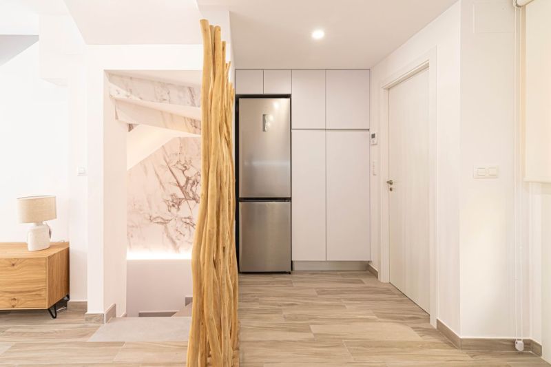 Innenraum einer Ferienwohnung mit Küchenschränken, Kühlschrank und Bodenbelag in Holzoptik.