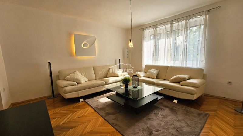 Wohnzimmer in einer 2-Zimmer-Wohnung mit weißem Sofa und Boden in Holzoptik.