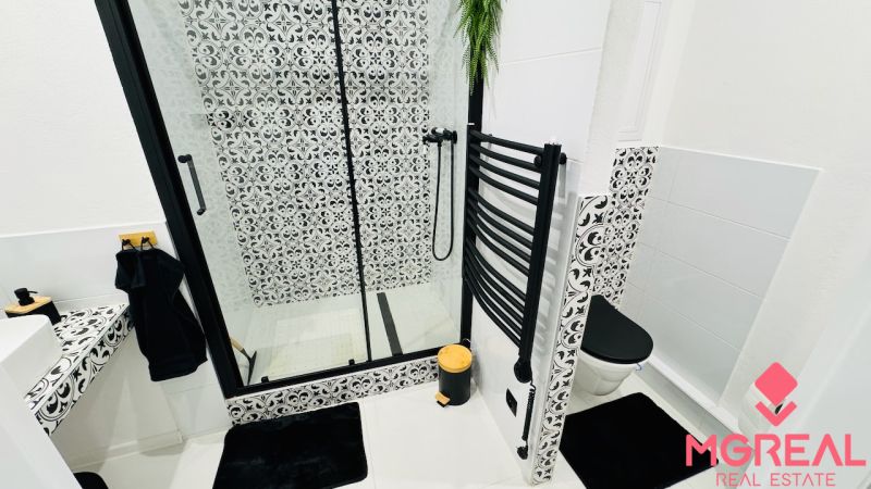 Badezimmer mit Duschkabine und schwarz-weißen Mustern in einer Einzimmerwohnung.