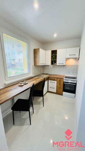 Küche in einer Einzimmerwohnung mit weißen Schränken und einem Boden in Holzoptik.