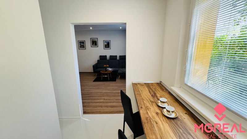 Innenraum einer Einzimmerwohnung mit Holzboden, Sofa und Tisch am Fenster.