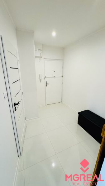 Weißer Eingangsflur mit Fliesen und dunkler Bank in einer Einzimmerwohnung.