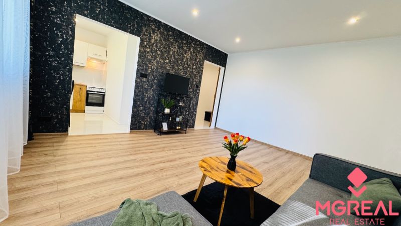Wohnzimmer einer Einzimmerwohnung mit Holzboden und Blumen auf dem Tisch.