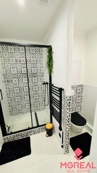 Badezimmer in einer Einzimmerwohnung mit schwarz-weißen Fliesen und hängendem Grün.