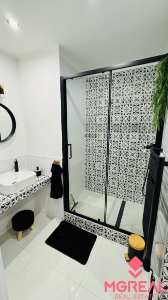 Badezimmer mit Duschkabine und gemusterten Fliesen in einer Einzimmerwohnung.