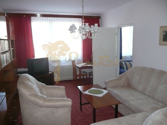 Wohnzimmer in einer Zweizimmerwohnung mit rotem Teppich und beigem Sofa.
