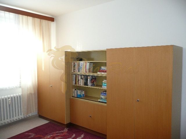 Ein Zimmer in einer 2-Zimmer-Wohnung mit einem Bücherregal und einem großen Schrank, Boden mit Holzdekor.