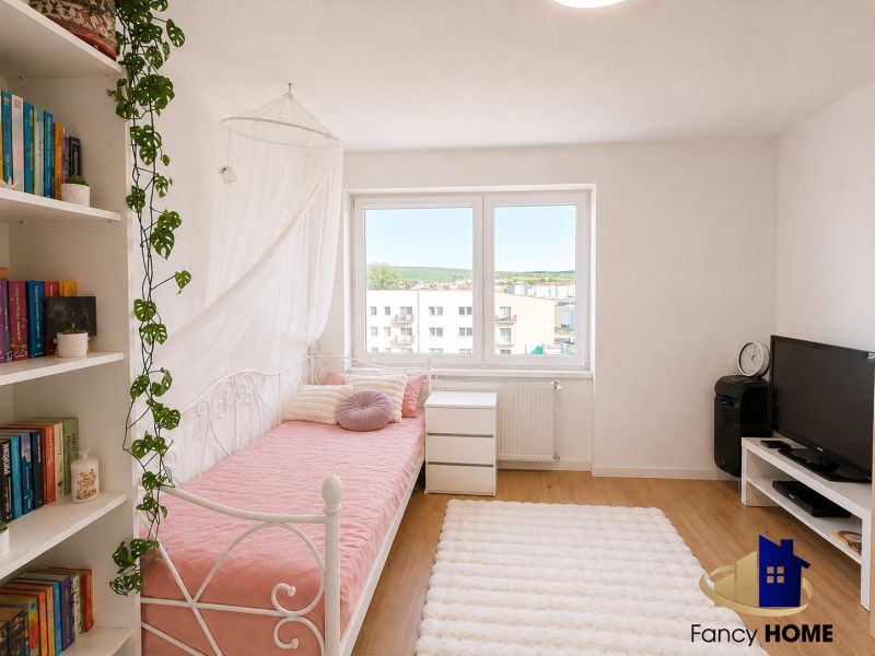 Ein Zimmer in einer 2-Zimmer-Wohnung mit einem Boden in Holzoptik, einem Bett und Regalen mit Büchern.