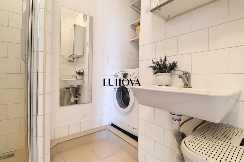 Badezimmer mit Waschmaschine, Waschbecken und Dusche in einer 2-Zimmer-Wohnung.