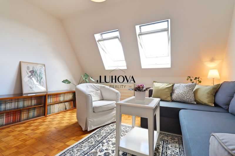 Wohnzimmer in einer 2-Zimmer-Wohnung mit Holzboden, bequemer Couch und Sessel.