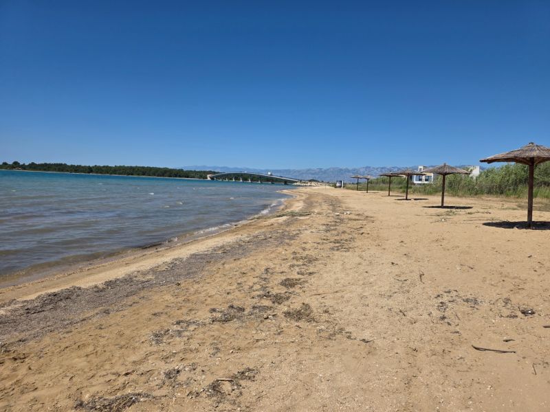 Sandstrand mit Strohdächern in Privlaka, mit blauem Himmel und Meer.