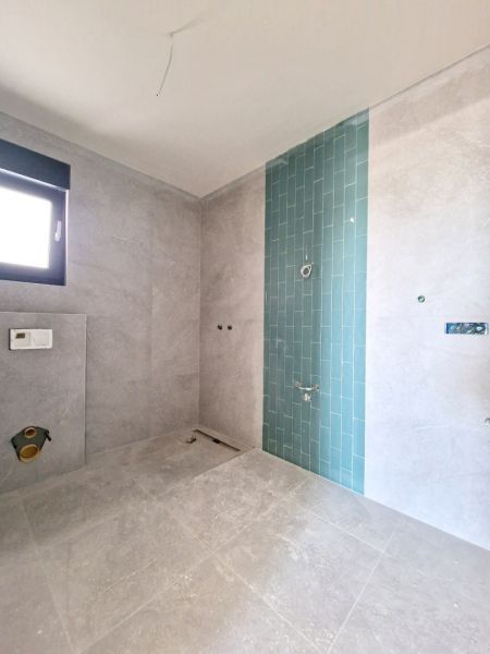 Badezimmer in einer 3-Zimmer-Wohnung mit grauen Fliesen und blauen Mosaiken an der Wand.