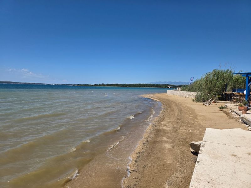 Ein Sandstrand am Meer in Privlaka mit klarem blauem Himmel und Wasser.