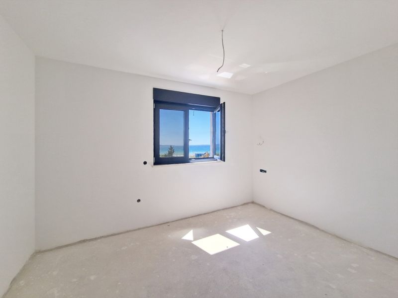 Ein leerer Raum ohne Möbel mit einem Fenster und Meerblick in einer 3-Zimmer-Wohnung.