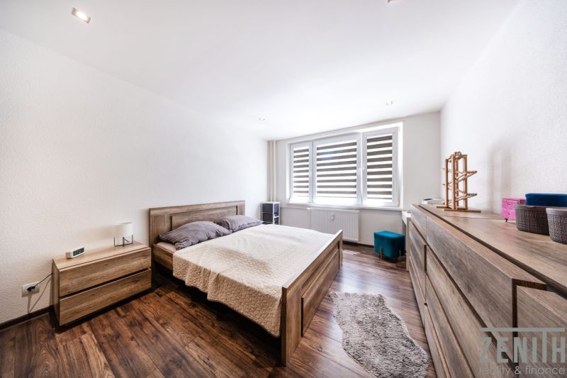 Schlafzimmer in einer 3-Zimmer-Wohnung mit Bett, Kommode und Boden in Holzoptik.