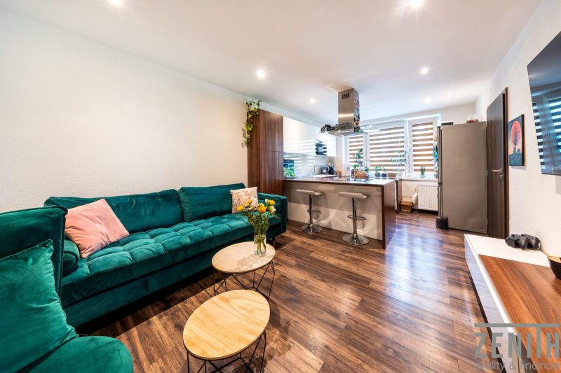 Wohnzimmer mit Küchenzeile in einer 3-Zimmer-Wohnung, Boden mit Holzdekor, grünes Sofa.