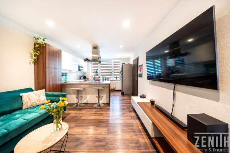 Wohnzimmer in einer 3-Zimmer-Wohnung mit Fernseher, Sofa und Küche, Boden mit Holzdekor.