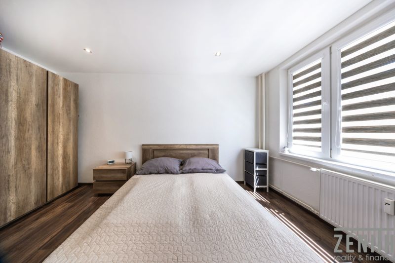Schlafzimmer mit Bett, Holzboden und großen Fenstern in einer 3-Zimmer-Wohnung.