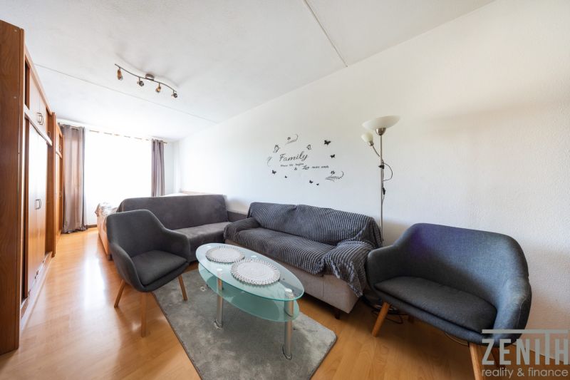 Wohnzimmer mit Holzboden in einer 3-Zimmer-Wohnung, graue Sofas, Glastisch.