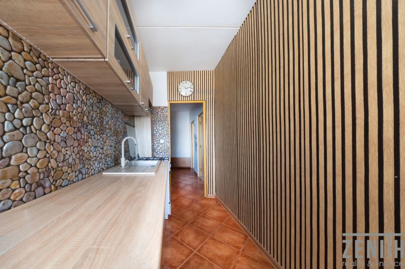 Küche mit Holzboden, Steinverkleidung und Schränken in einer 3-Zimmer-Wohnung.