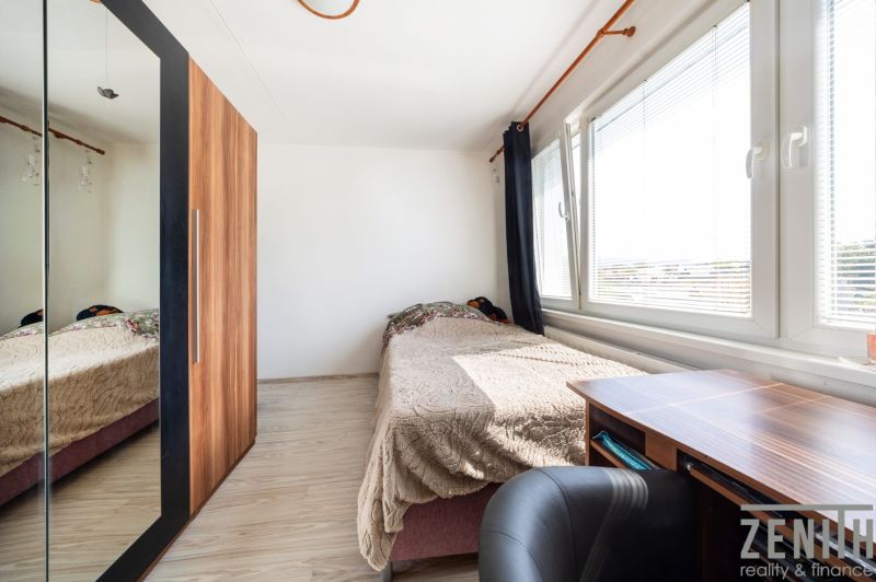 Ein Zimmer mit einem Bett, einem Schreibtisch und einem Schrank mit Spiegel in einer 3-Zimmer-Wohnung.