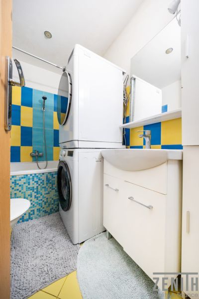 Badezimmer in einer 3-Zimmer-Wohnung mit Waschmaschine, Trockner und bunten Fliesen.
