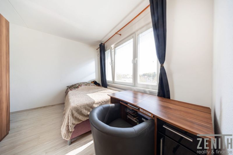 Ein Zimmer in einer 3-Zimmer-Wohnung mit Bett, Tisch und Fenstern mit dunklen Vorhängen.