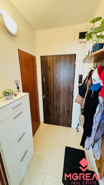 Einfacher Flur einer Einzimmerwohnung mit Fliesenboden, Schuhschrank und Kleiderhaken.