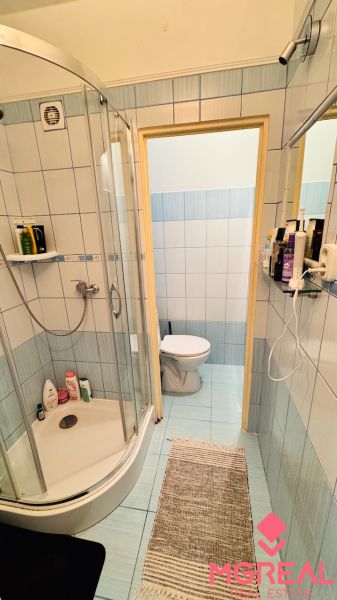 Badezimmer in einer Einzimmerwohnung mit einer durchsichtigen Duschkabine und hellblauen Fliesen.