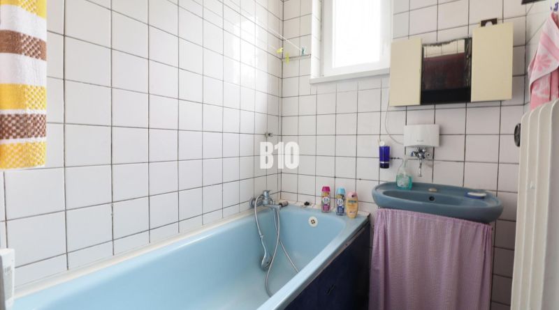 Badezimmer mit Badewanne und Waschbecken in einem Einfamilienhaus. Weiße Fliesen und hellblaue Badewanne.