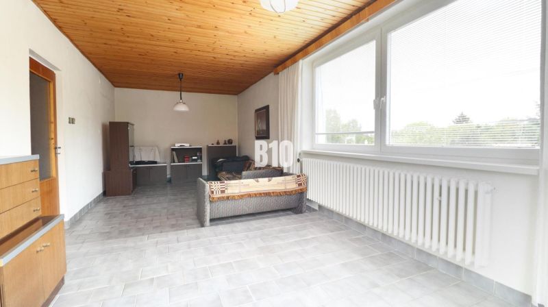 Wohnzimmer mit Holzdecke, Sofa, großem Fenster und hellgrauem Boden.