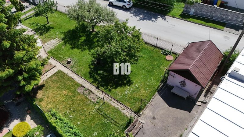 Ein Garten mit Rasen bei einem Einfamilienhaus in Martin, man sieht einen Baum, einen Gartenweg und einen Unterstand.