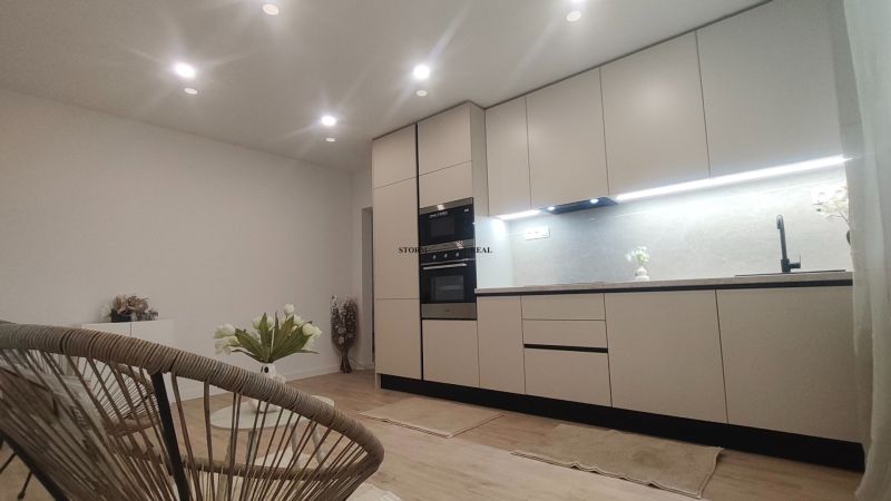 Küche in einer 4-Zimmer-Wohnung mit Holzboden, weißen Schränken und Pflanzen.