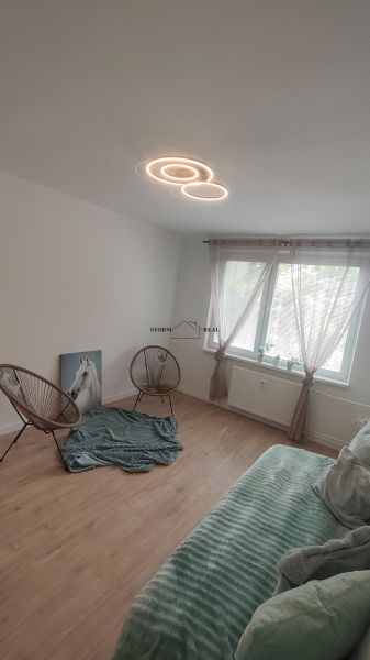 Izba in einem 4-Zimmer-Wohnung mit Holzboden, Sesseln und einem Sofa.